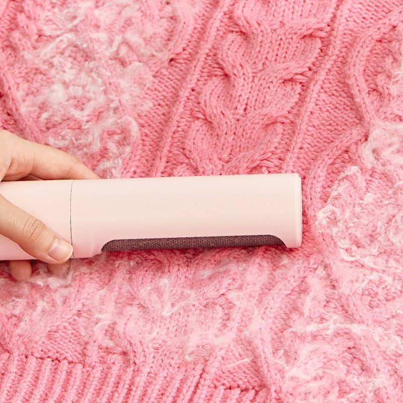 Pink lint roller brush gliding over a knit sweater to lift pet hair