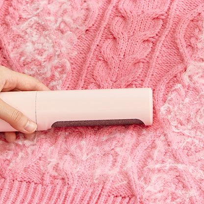 Pink lint roller brush gliding over a knit sweater to lift pet hair