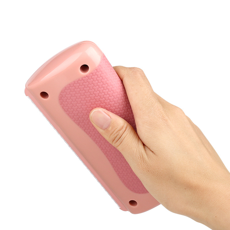 Pink pet grooming comb held in hand, textured grip and teeth edge visible
