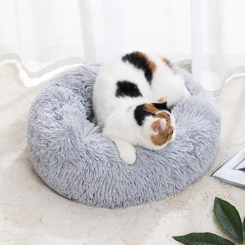 Plush round donut pet bed in light gray, with a small calico cat curled inside.