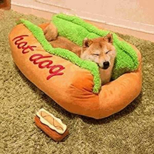 Hot dog-shaped pet bed, orange plush with green top insert and red 'hot dog' embroidery.