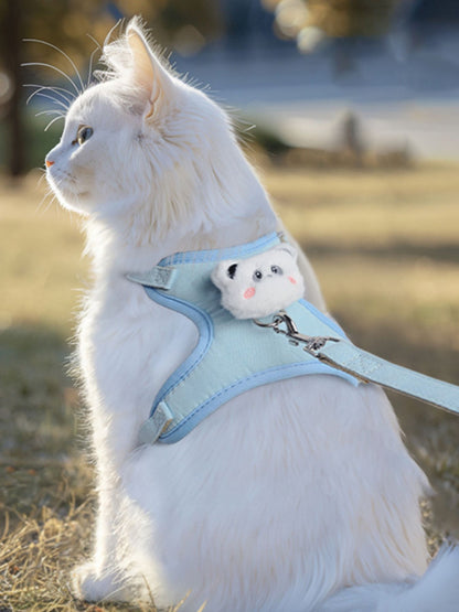 Light blue pet harness with plush bear face patch and leash ring, on a white cat