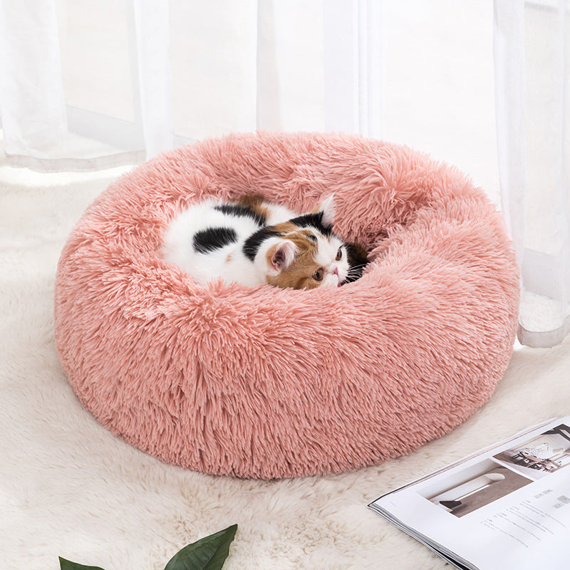 Plush round donut pet bed in pink, with a small cat curled inside.