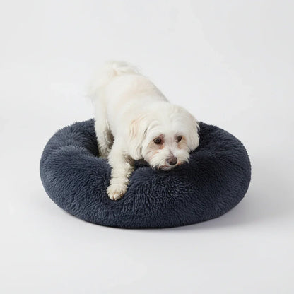 Small white dog resting in a Midfox plush donut comfort pet bed in navy blue.