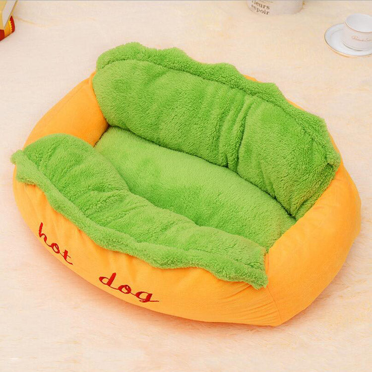 Hot dog-shaped pet bed with green padded top and orange sides, red 'hot dog' embroidery.
