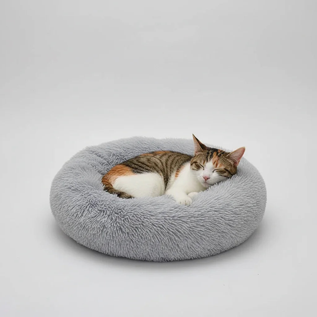 A calico cat sleeping peacefully in a grey Midfox Plush Donut Comfort Pet Bed.