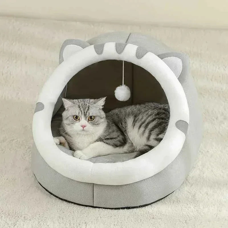 A grey tabby cat resting inside a WTN Essentials Cozy Cave Cat Bed with a hanging toy.