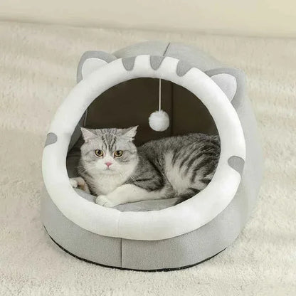 A grey tabby cat resting inside a WTN Essentials Cozy Cave Cat Bed with a hanging toy.