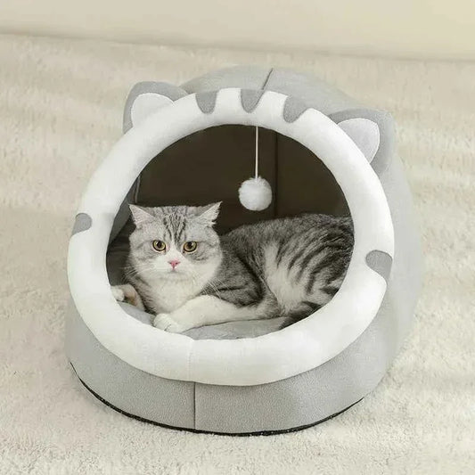 A grey tabby cat resting inside a WTN Essentials Cozy Cave Cat Bed with a hanging toy.