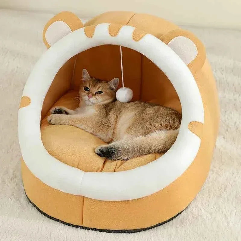Ginger cat lounging in a WTN Essentials Cozy Cave Cat Bed with a hanging toy.