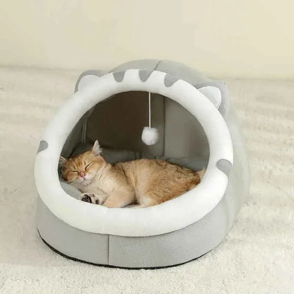 Ginger cat sleeping inside a grey WTN Essentials Cozy Cave Cat Bed with a hanging toy.