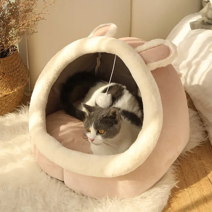 Close-up of plush cat cave bed entrance with cream lining and hanging pom-pom