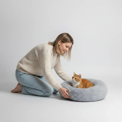 A woman placing an orange cat in a grey Midfox Plush Donut Comfort Pet Bed