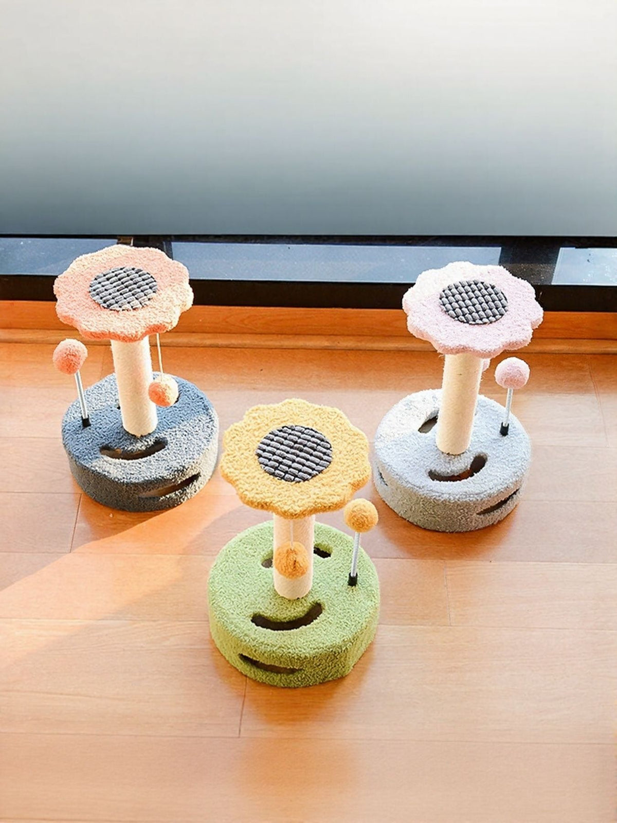 Three cat scratching posts with dangling balls, gray bases with pink and yellow flower tops.