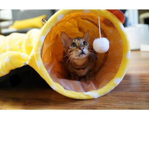 Pink plush cat tunnel bed with circular entrance and hanging white pom-pom