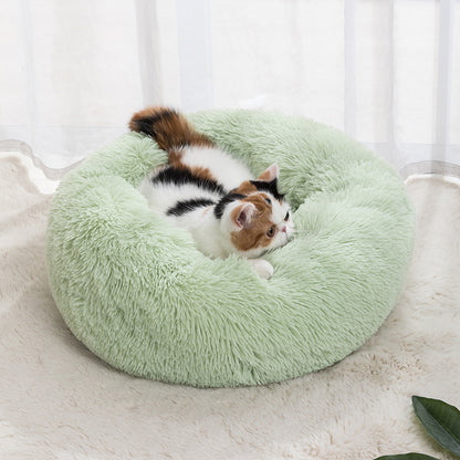 Plush round donut pet bed in light green, with a small calico cat curled inside.