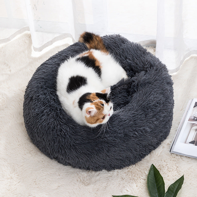 Plush round donut pet bed in dark gray, with a small calico cat curled inside.