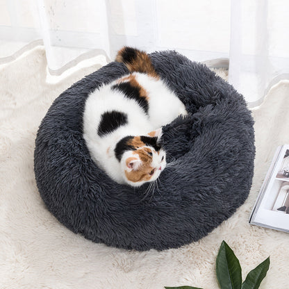 Plush round donut pet bed in dark gray, with a small calico cat curled inside.
