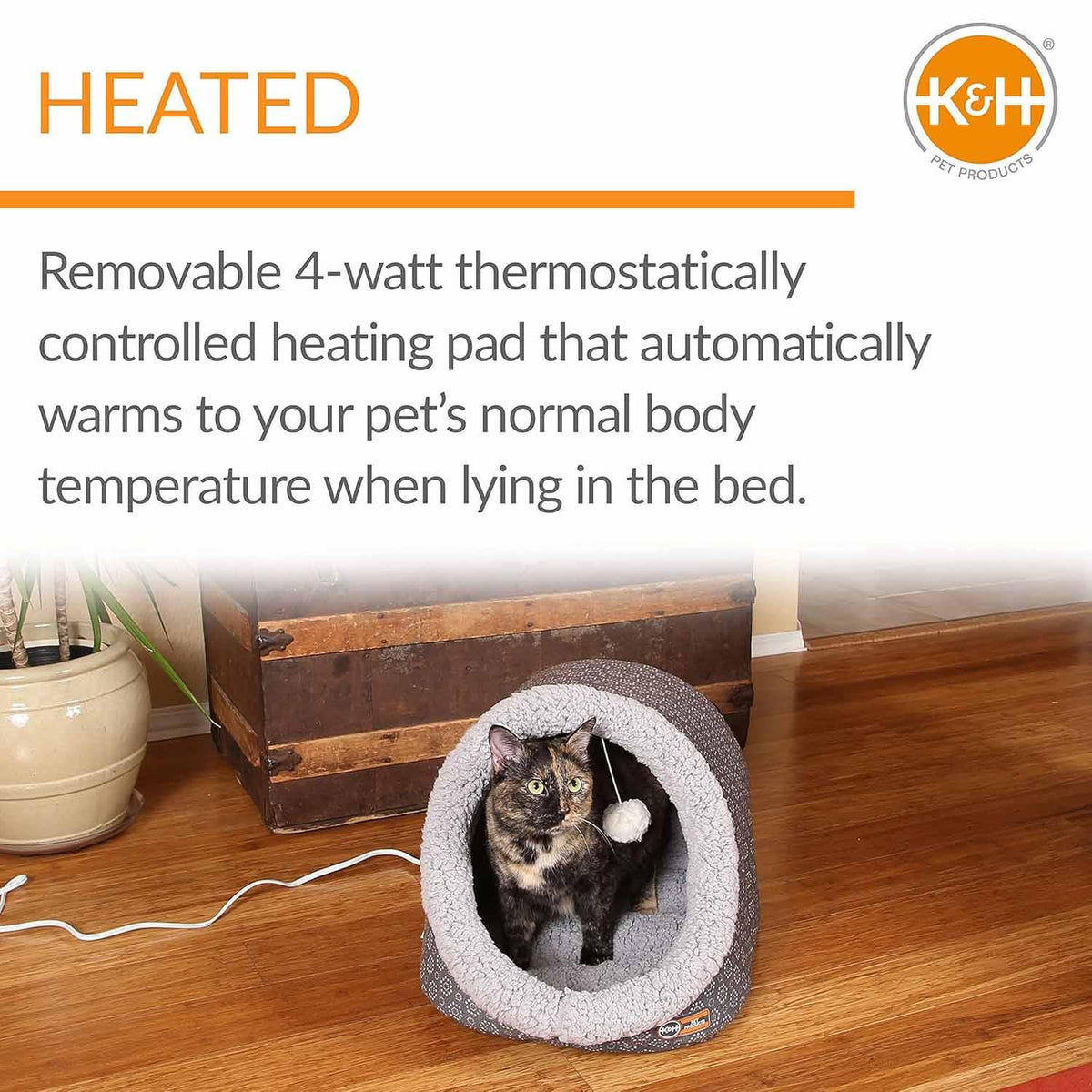 Tortoiseshell cat resting inside a plush Jeffers heated cat cave bed on a wooden floor.