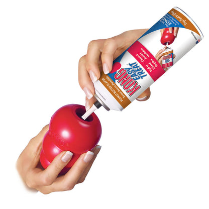 Red KONG Classic rubber dog chew toy with treat being inserted by hands.